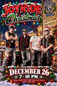 Joyride band photo: four band members in Santa hats and sunglasses wrapped in Christmas lights, posed in front of a snowy, lit-up building